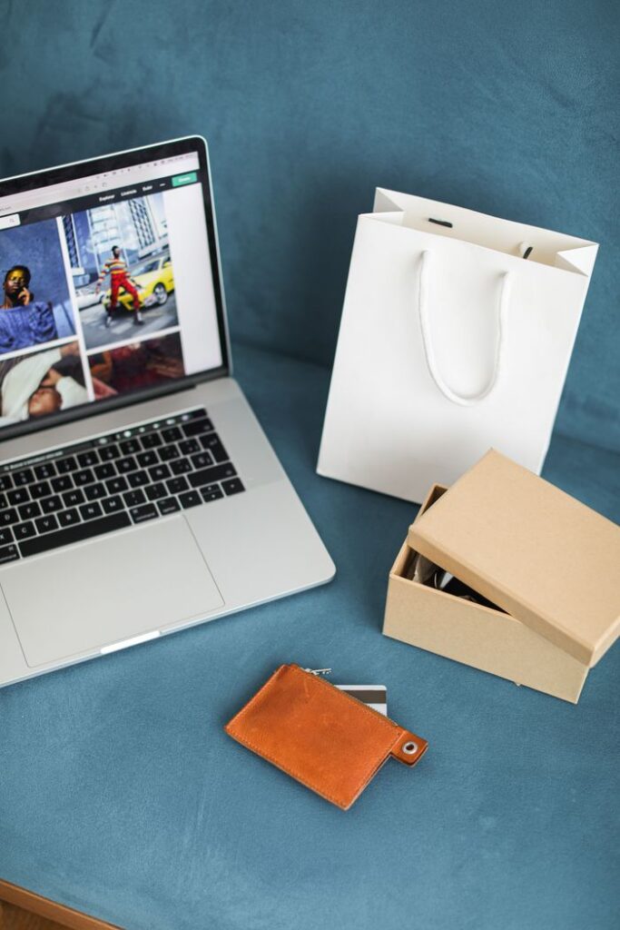 A high-angle view of online shopping items including a laptop, gift bags, and wallet on a blue surface.